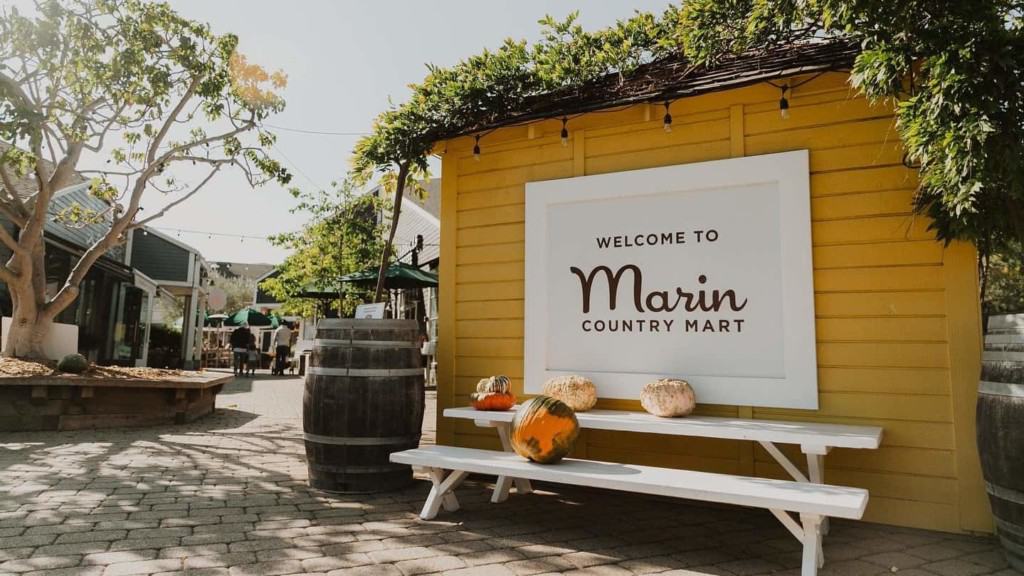 picnic table and wine barrel with decorative pumpkins in from of Marin Country Mart sign