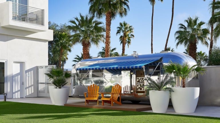 Airstream trailer with blue awning surrounded by palm trees