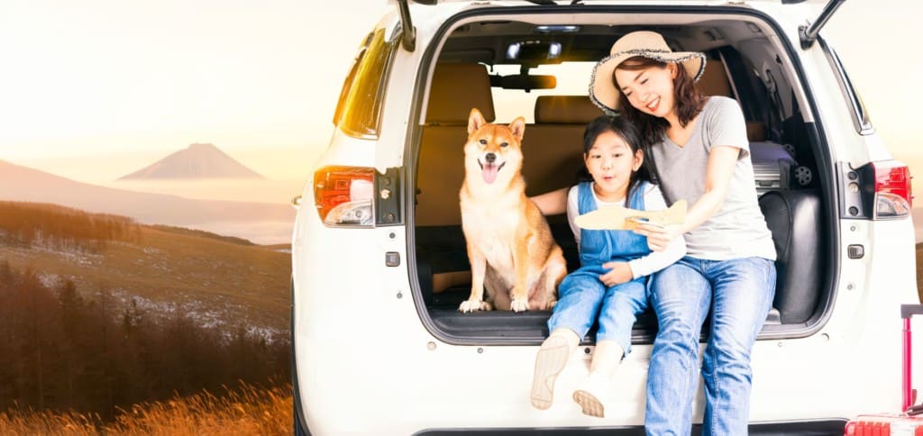 Mother and daughter with shiba inu dog sit on tailgate of white SUV