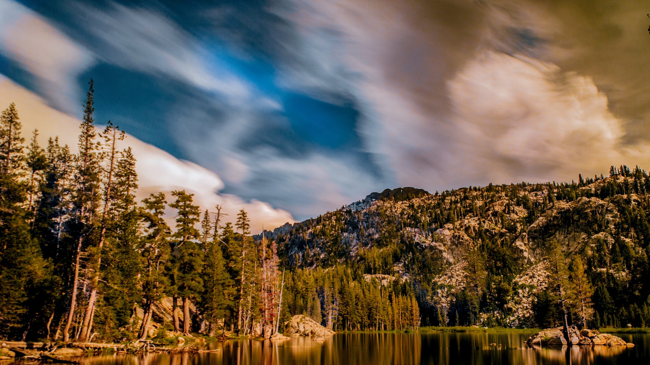 Discover a serene lake surrounded by tall evergreen trees and rugged mountains off Highway 88. Dramatic, swirling clouds fill the sky with occasional hints of blue, providing a stunning view. Perfect for outdoor activities with your dog.