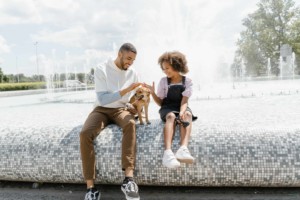 man and girl sit on ledge of fountain with dog