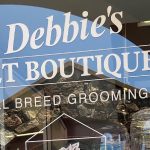 Debbie's Pet Boutique in Healdsburg draws attention with its storefront display, prominently advertising "All Breed Grooming." The window is filled with an array of pet products, each item carefully arranged to catch the eye of passersby. A large poster stands out, highlighting PureVita pet food. The poster includes vibrant images of happy dogs and details about the nutritional benefits of the food, making it clear that health and quality are priorities at this shop.