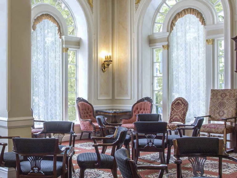 Formal Beresford Arms room with large arched windows, lace curtains, ornate chairs, and patterned carpet; dogs not allowed.