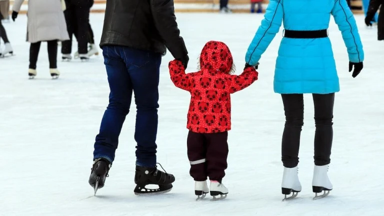 A little boy with his parents skates on the rink in the winter. Active family sport, winter holidays, sports clubs.