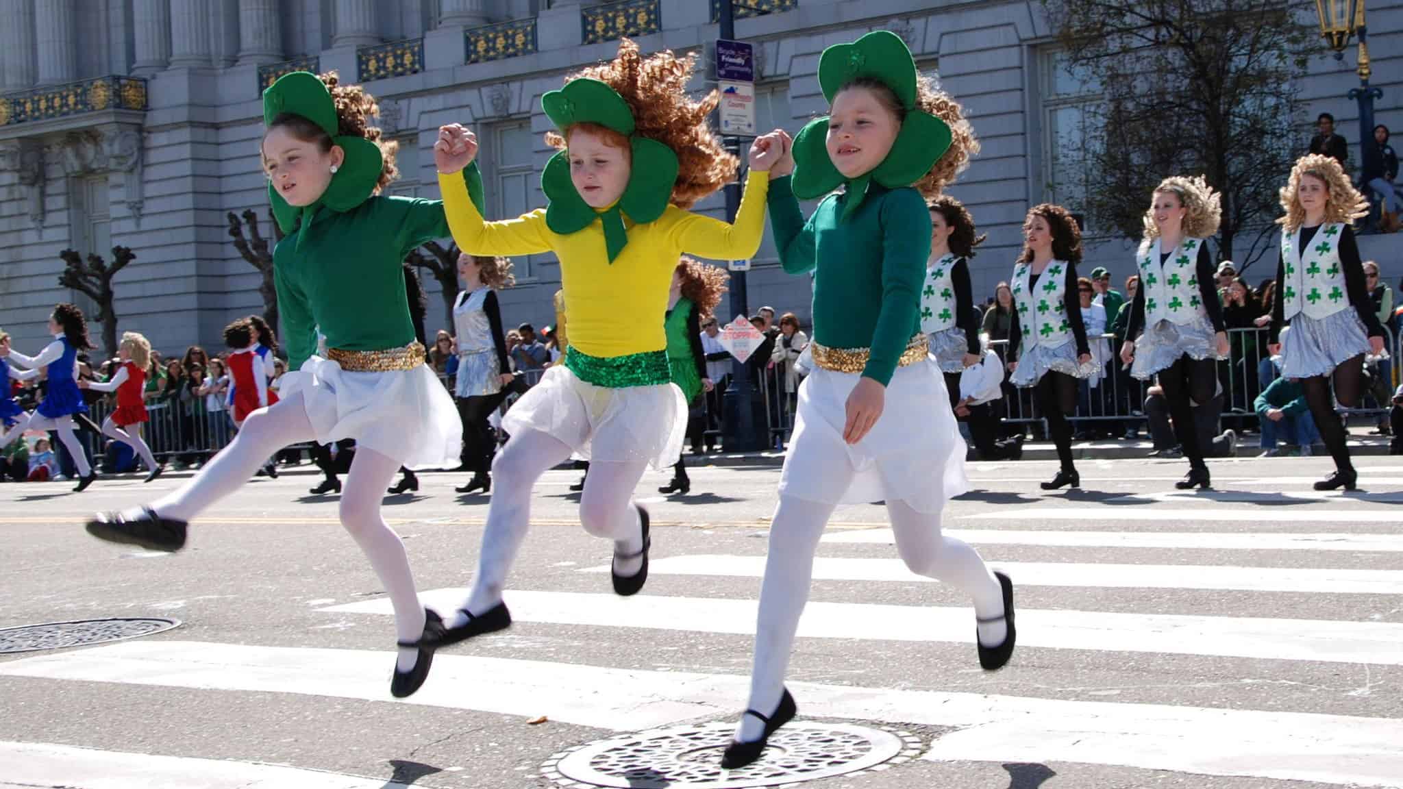 3 red haired girls wearing shamrock head pieces jumping