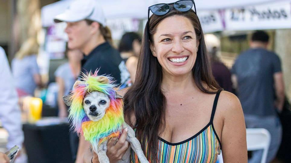 woman holding a chihuahua wearing a faux fur rainbow costume