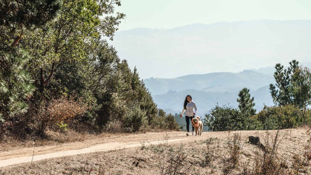 woman hiking with dog on dirt path