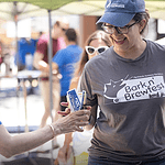 At the Bark n' Brewfest, a woman is cheerfully handing a drink to another woman amidst the lively outdoor event. - Dogtrekker