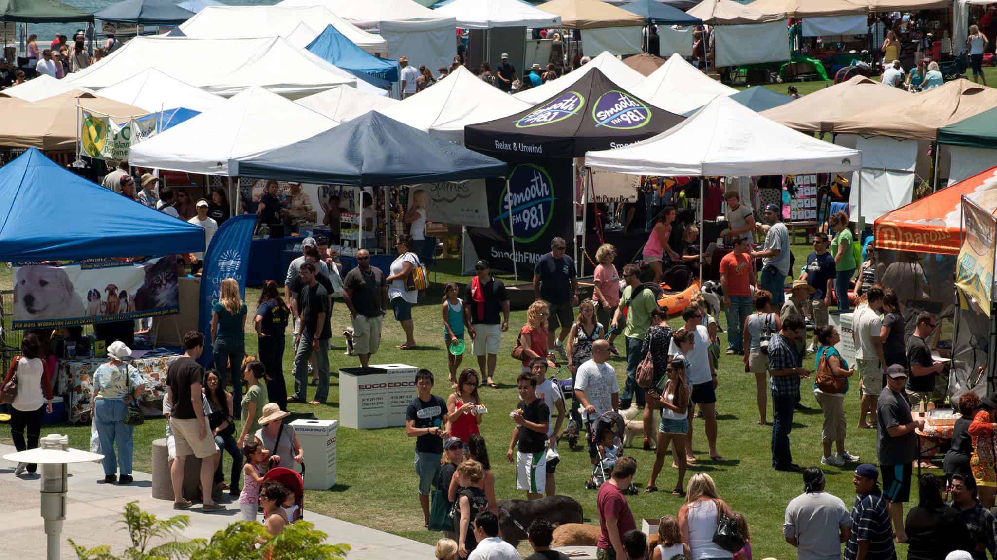 a crowd of people and dogs standing around tents in a field.