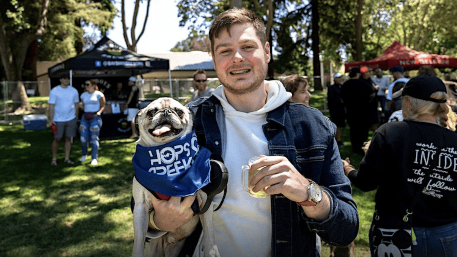 man holding dog in one arm and beer in the other at Hops & Creek Brewfest.