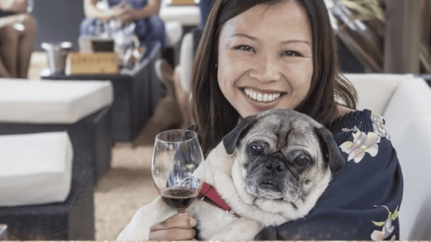 a woman holding a dog and a glass of wine.