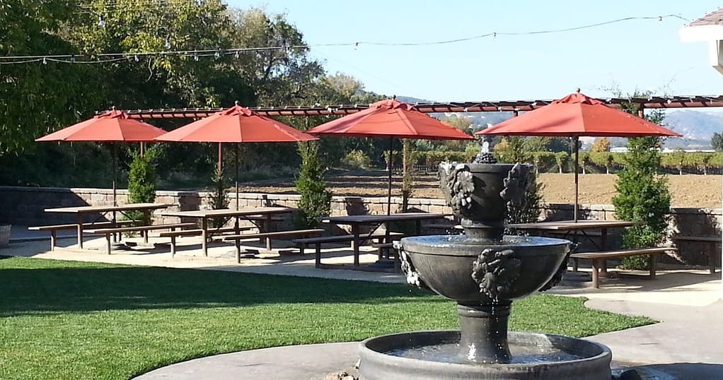 a fountain in the middle of a park with red umbrellas.