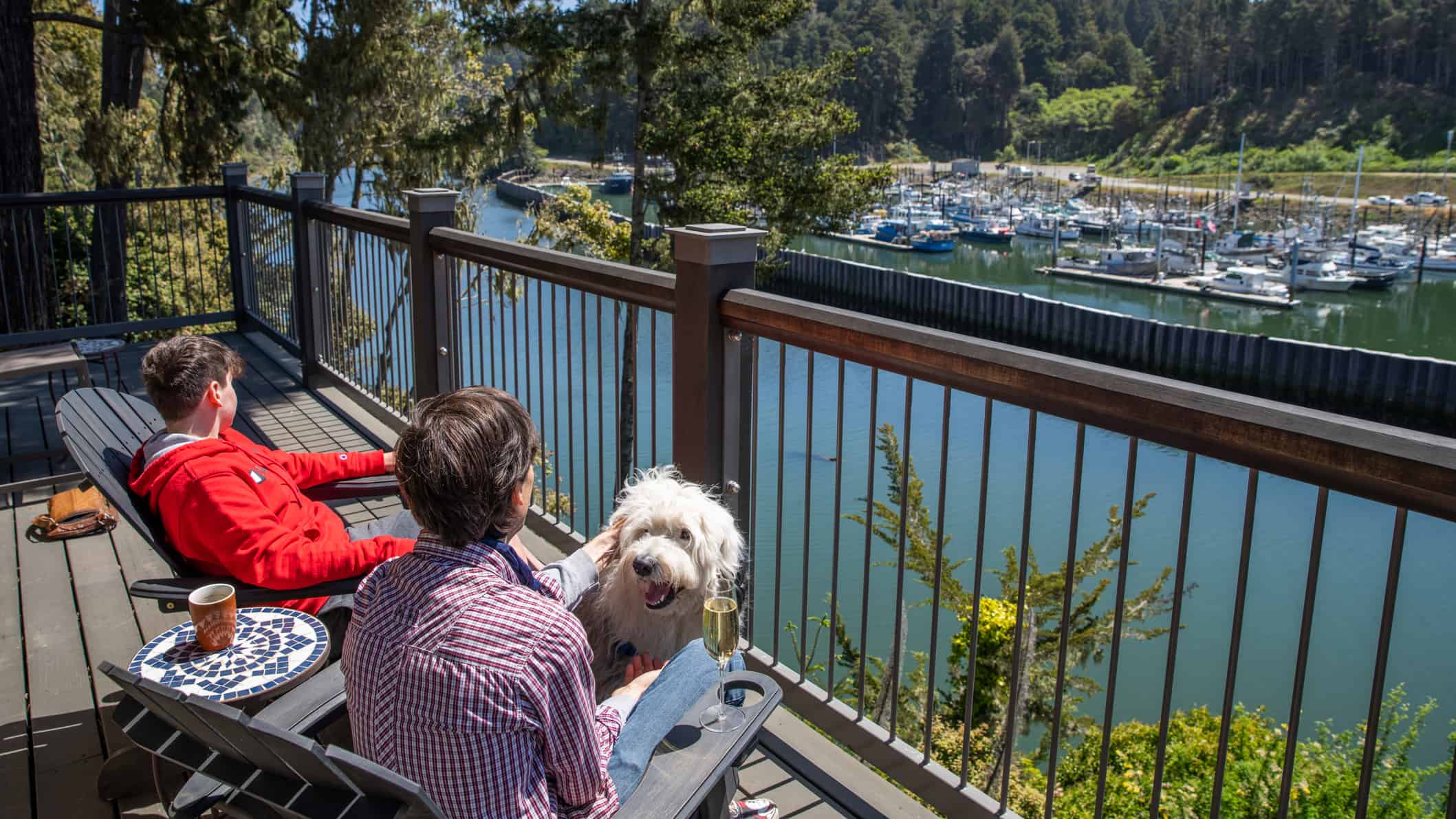 2 men and a dog sit on a deck overlooking the water at Noyo Harbor Inn.