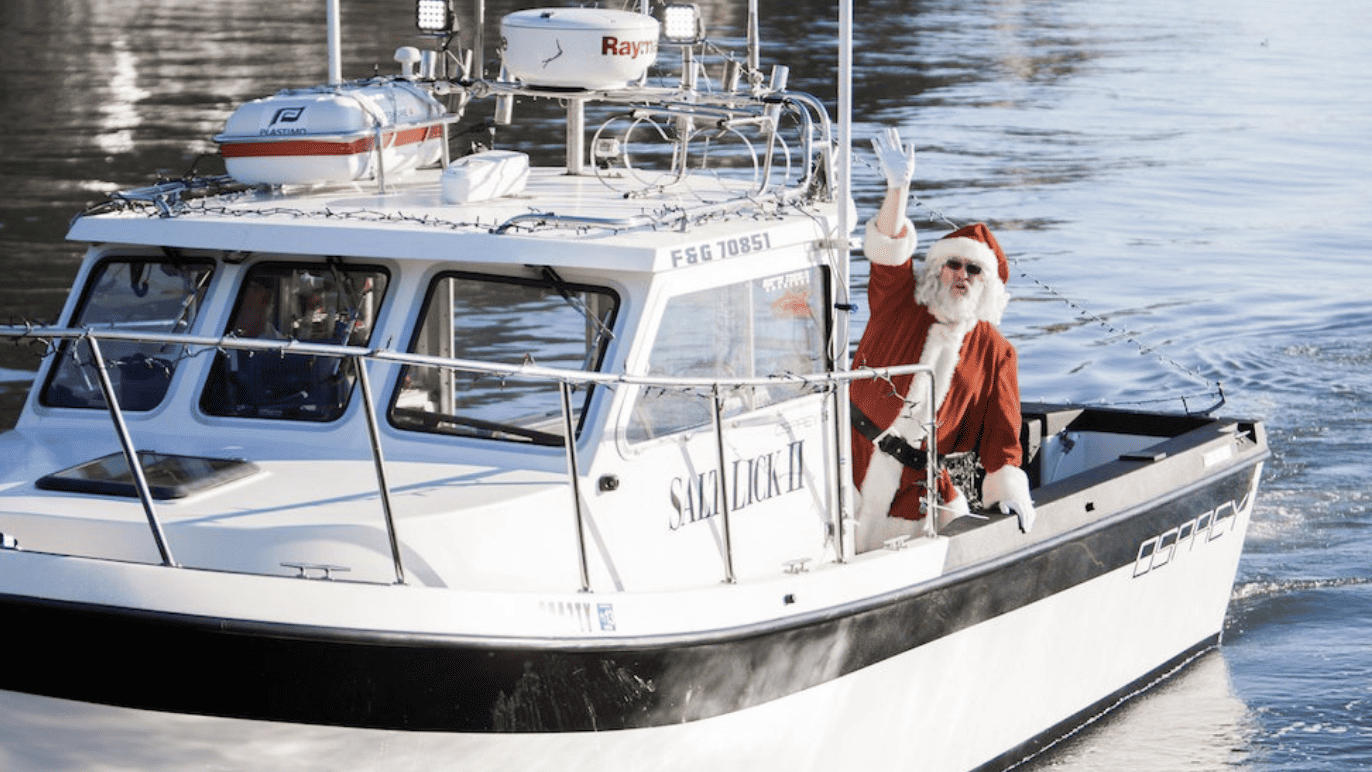 Santa waves from a boat on the water.