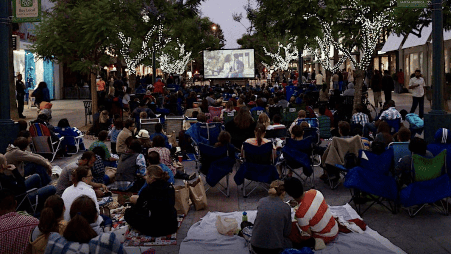 crowd sitting in front of an outdoor movie screen