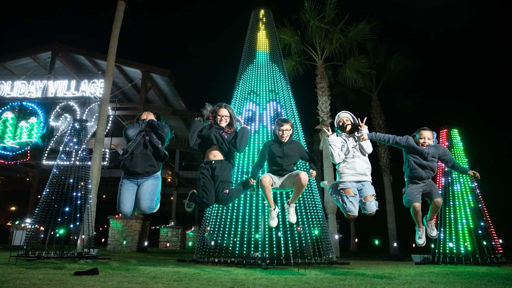 kids jumping in front of illuminated Christmas light display at night