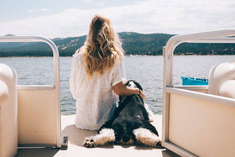A woman sits on the back of a boat with her dog at Big Bear Lake.