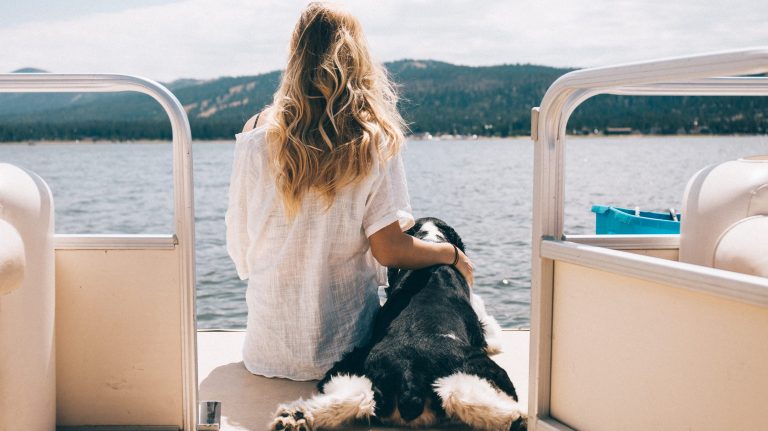 A woman sits on the back of a boat with her dog at Big Bear Lake.