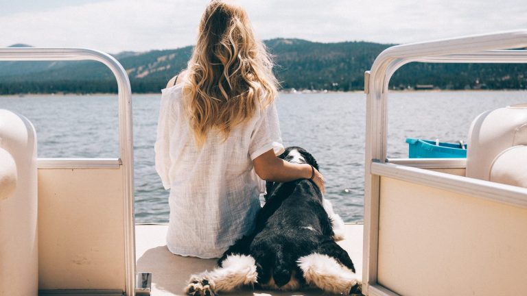 A woman sits on the back of a boat with her dog at Big Bear Lake.