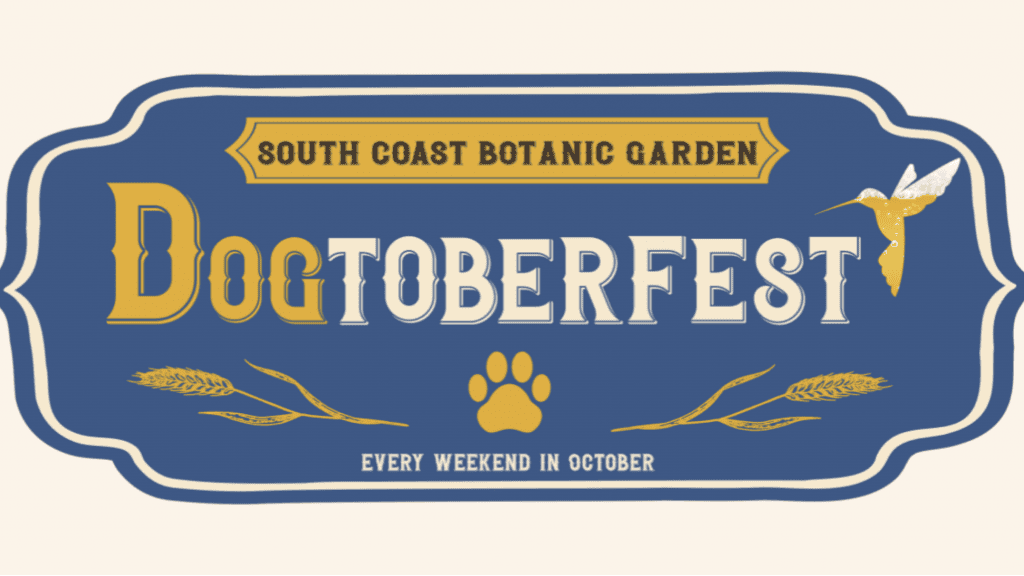 A blue sign with white and yellow text announces "South Coast Botanic Garden Dogtoberfest." The event features a dog paw print and wheat sprigs as decorative elements. The pet festival takes place every weekend in October.