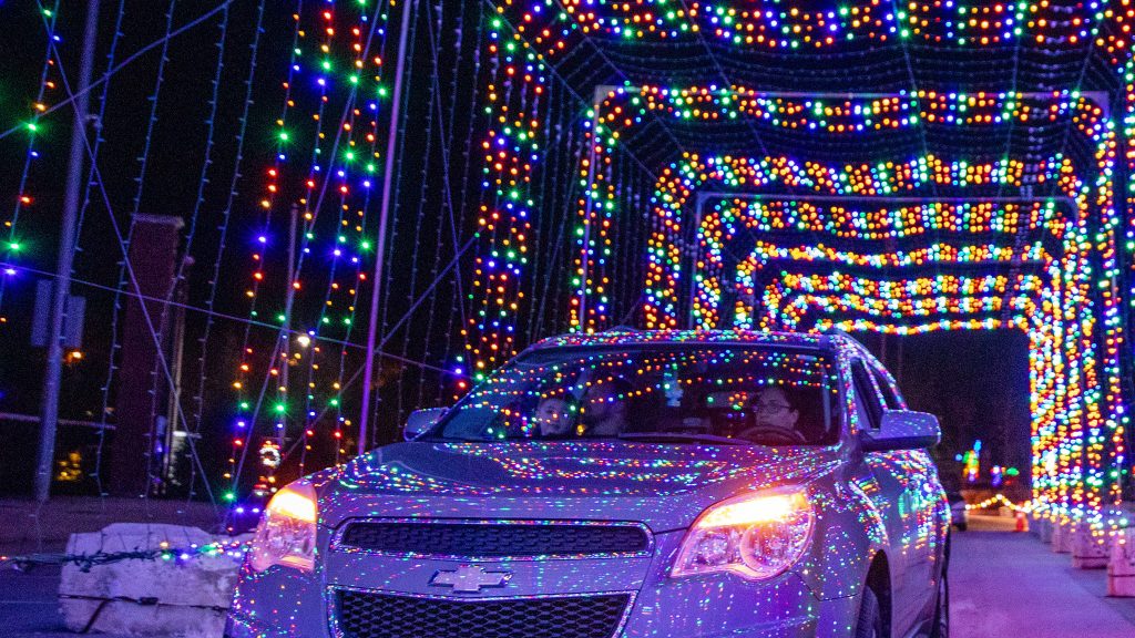 As you drive through the tunnel, countless multicolored Christmas lights create a vibrant display around your car. The glowing reds, greens, and blues splash across the vehicle's surface, bathing the surroundings in a striking festive glow. It's an immersive experience of light and color that adds a magical flair to your journey with your dog by your side.