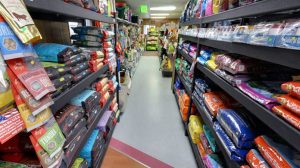 In the busy pet market, an aisle beckons with shelves packed full of brightly colored pet food bags on either side. The area is well-lit, making the vivid hues of various pet care products stand out invitingly.
