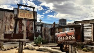 A visit to the Joshua Tree Saloon offers a genuine taste of the Old West. The saloon's weathered facade, with its sun-bleached wood and rustic charm, stands starkly against the deep blue desert sky. Corrugated metal sheets and timeworn wooden structures surround the area, seamlessly blending into the rugged landscape. Cactus plants add a spiky green contrast to the dusty earth tones. It's a scene that encapsulates both history and adventure—perfect for a memorable outing with your canine companion as you explore all that Joshua Tree has to offer together.