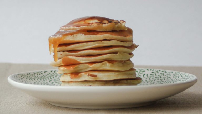 A stack of six pancakes is artfully arranged on a white plate adorned with a lively green leaf pattern. The syrup cascades down the sides, inviting your canine companion to join the fun after a satisfying breakfast. This image might spark memories of Sunday mornings in Inland Mendocino County, but it’s an inspiration for planning your next adventure with your dog—be it exploring nature trails, visiting pet-friendly cafes, or lounging at home concocting pancake recipes safe for dogs to enjoy.