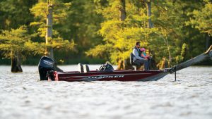 A vibrant dog park bathed in sunlight features abundant greenery with mature trees, offering ample shade for leisurely outdoor activities. In the distance is a well-equipped playground that presents an additional activity area. An inviting picnic table spreads out nearby, ideal for enjoying meals al fresco or taking relaxing breaks from play. A neatly-placed trash bin aids in maintaining the park's cleanliness for everyone's enjoyment. Dominating the scene is a generously wide dirt path gracefully curving through the expanse of grass, promising exploratory walks and lively fetch games.