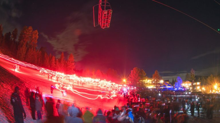 Nighttime ski lift with red lights, crowds of people at a ski resort, and vibrant light trails creating a lively winter scene; perfect for winter sports enthusiasts and adventure lovers.