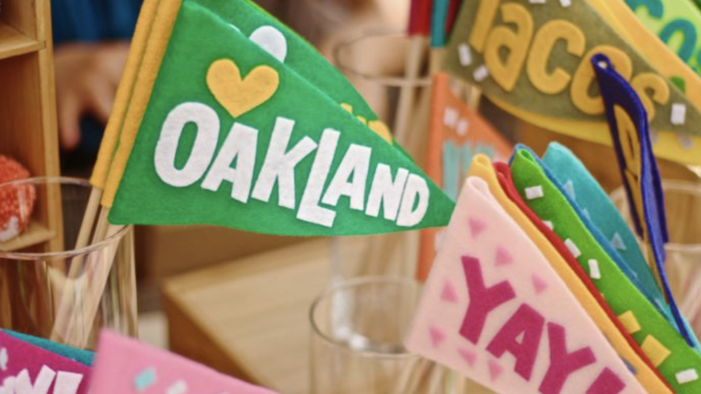 Colorful felt dog-themed travel pennants with "Oakland" on one of them, displayed in a shop setting; festive, vibrant, perfect for dog lovers and travel enthusiasts.